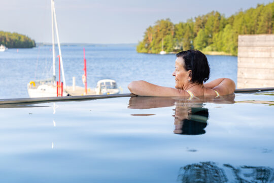 Ilola Inn Infinity Pool Sysmässä, nainen nojailee uima-altaan reunaan ja katselee aurinkoiselle Päijänteelle