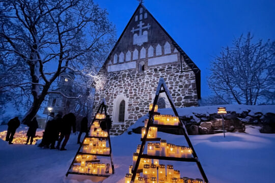 Hollolan keskiaikainen kirkko talvimaisemassa iltavalossa kynttilöineen.