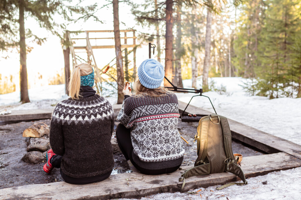 Kaksi retkeilijää istumassa nuotiolla talvella