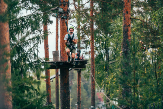 Liikuntakeskus Pajulahti, Pajulahden Seikkailupuisto. Mies liukumassa köysirataa pitkin korkealla puiden välissä.