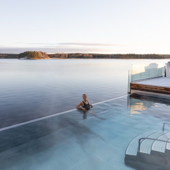 Nainen Aisti Sauna & Span infinity-altaassa. Taustalla tyyni Päijänne. Terassilla lunta.